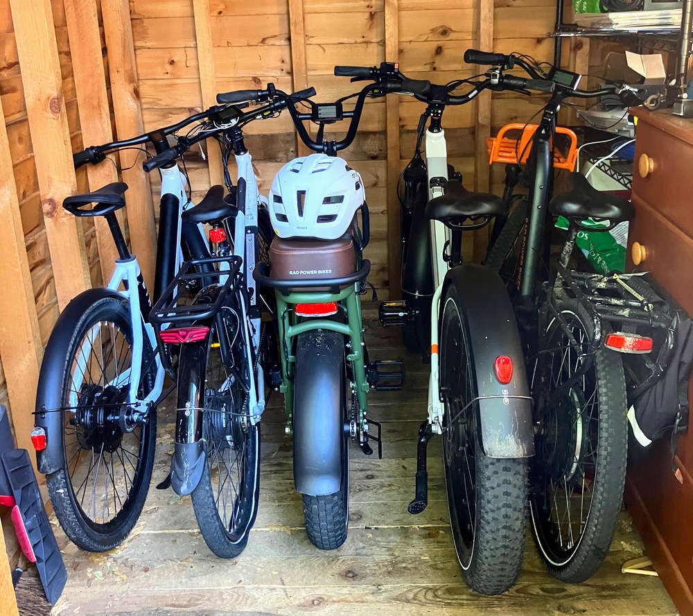 A group of four ebikes standing up in the inside of a wooded shed.
